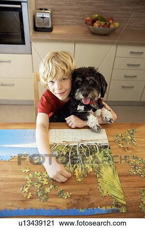 Stock Image - A boy holding a dog while doing a puzzle. Fotosearch