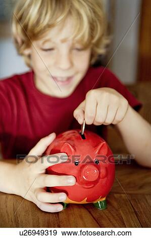 Stock Photo - A boy putting money in a piggy bank. Fotosearch