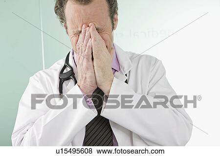 A doctor holding his hands over his face View Large Photo Image Stock Photo - A doctor holding his hands over his face. Fotosearch
