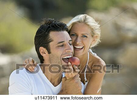 Stock Image - A female feeding a latin man a nectarine. Fotosearch