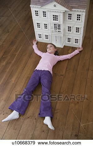 Stock Photo - A girl lying in front of her dollhouse.. Fotosearch