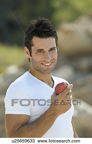 Stock Image - A latin male holding an apple smiling. Fotosearch