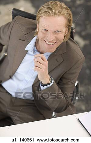 A Mid-40 Businessman sitting at a desk View Large Photo Image Stock Image - A Mid-40 Businessman sitting at a desk. Fotosearch