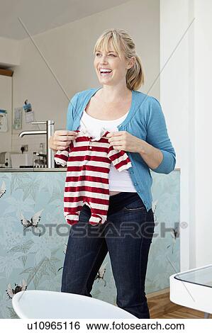 Stock Photograph - A young pregnant mum holding a baby grow. Fotosearch
