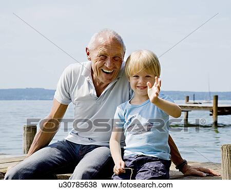 Stock Photo - boy with grandfather on pier at lake. Fotosearch