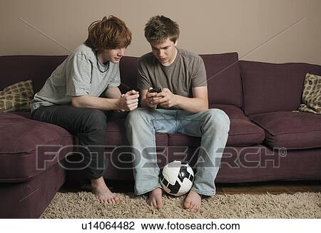 Stock Image - Boys sending message from mobile phone. Fotosearch