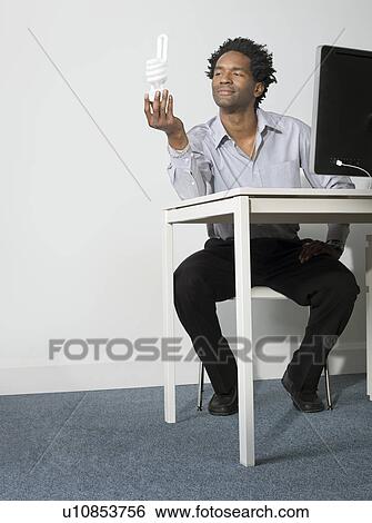 Stock Photograph - Business man holds up eco lightbulb. Fotosearch