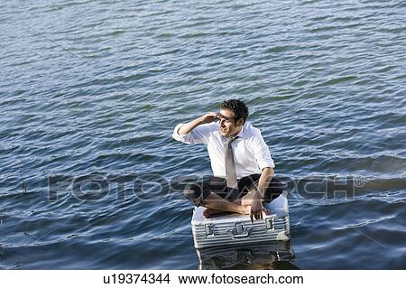 Picture - businessman sitting on floating suitcase. Fotosearch