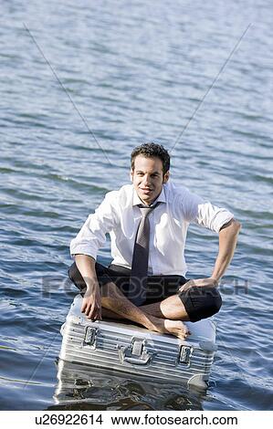 Picture - businessman sitting on floating suitcase. Fotosearch