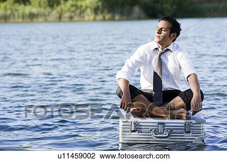 Stock Image - businessman sitting on floating suitcase. Fotosearch