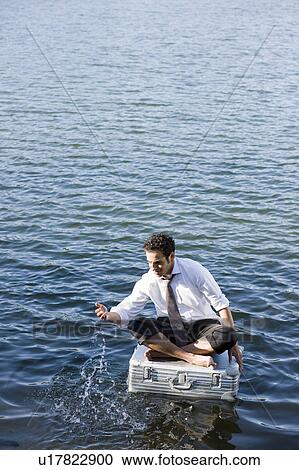 Stock Image - businessman sitting on floating suitcase. Fotosearch