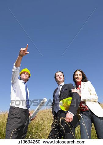 Stock Image - contractors with blueprints in field. Fotosearch