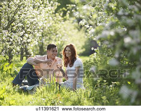 Stock Image - Couple Having Picnic In Orchard. Fotosearch