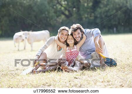 Stock Image - Family sitting laughing hugging in field. Fotosearch