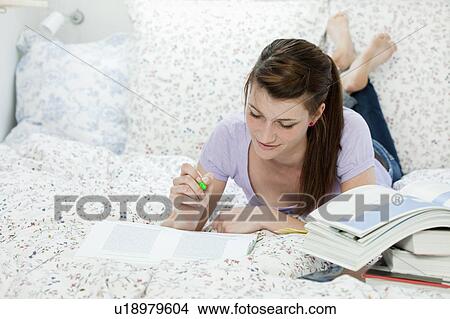 Picture - Female student lying in bed, learning. Fotosearch