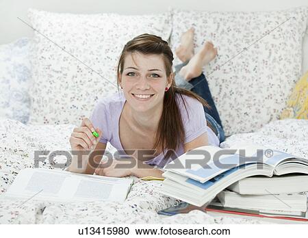 Stock Image - Female student lying in bed, learning. Fotosearch
