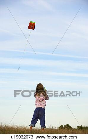 Girl flying a kite in a field View Large Photo Image Stock Image - Girl flying a kite in a field. Fotosearch