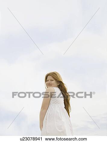 Stock Image - Girl Looking to camera set against sky. Fotosearch