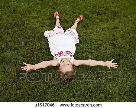 Stock Image - Girl lying arms outstretched on a lawn. Fotosearch
