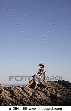 Stock Photography - Girl sitting on rocks by the sea. Fotosearch