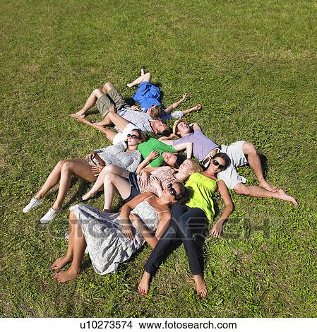 Picture - group of young people lying in field. Fotosearch