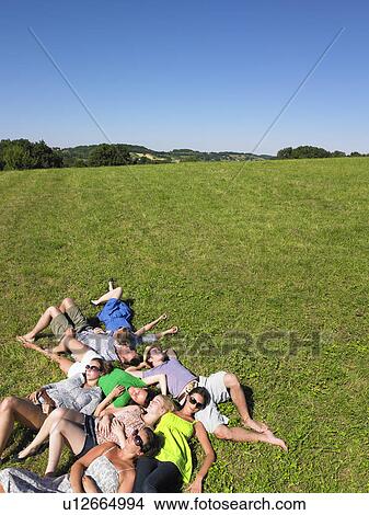 Picture - group of young people lying in field. Fotosearch