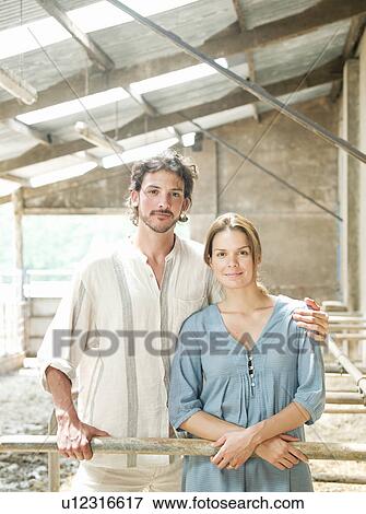 Stock Photo - Man and woman standing in cattle shed. Fotosearch