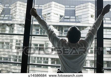 Picture - man at window with raised arms. Fotosearch