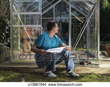 Picture - Man building greenhouse in garden. Fotosearch