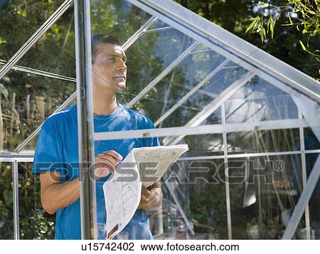 Stock Image - Man building greenhouse in garden. Fotosearch