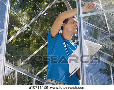 Stock Photo - Man building greenhouse in garden. Fotosearch