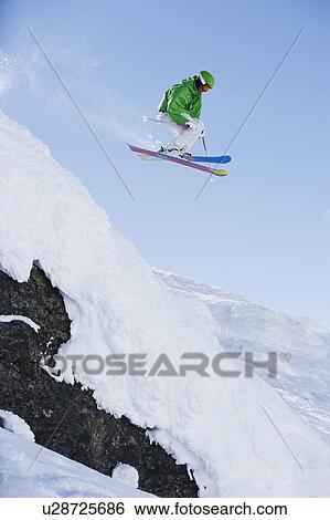 Stock Photograph - Man in green dropping a cliff face.. Fotosearch