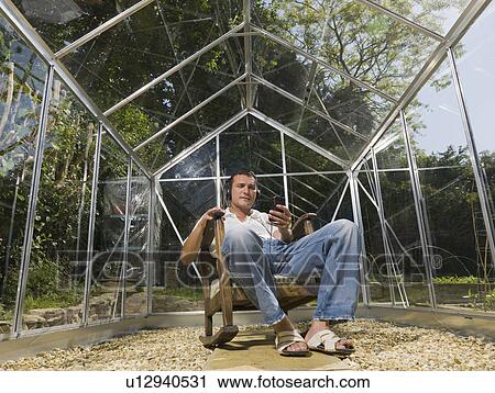 Stock Image - Man in greenhouse with headphones. Fotosearch