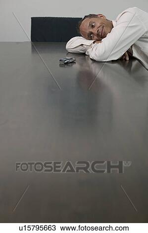 man leaing on table looking at phone View Large Photo Image Stock Image - man leaing on table looking at phone. Fotosearch