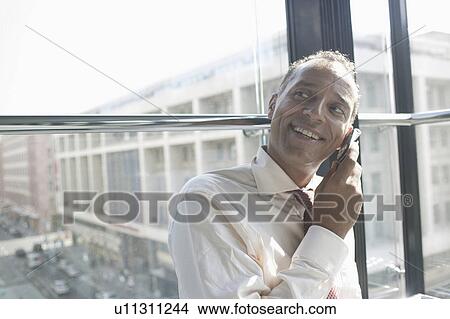 Picture - man leaning at window using cell phone. Fotosearch