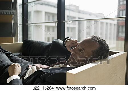 Picture - man lying on sofa using cell phone. Fotosearch