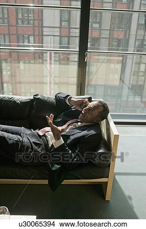 Picture - man lying on sofa using cell phone. Fotosearch