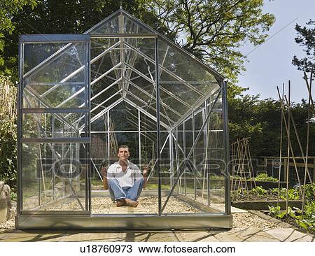 Stock Image - Man meditating in greenhouse in garden. Fotosearch