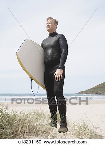 Stock Image - Man on dunes with surfboard. Fotosearch