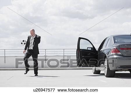 Stock Photo - man playing football near car. Fotosearch