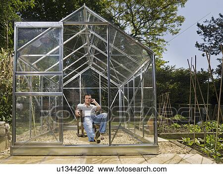 Stock Image - Man relaxing in greenhouse with music. Fotosearch