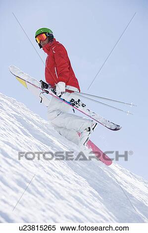 Stock Photography - Man sin red carrying skis uphill.. Fotosearch