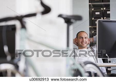 Stock Image - man sitting at desk relaxing. Fotosearch