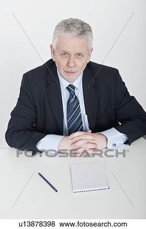 Stock Photo - man sitting at table, hands clasped. Fotosearch