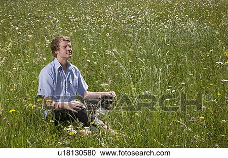 Stock Image - man sitting in grass with spring flowers. Fotosearch
