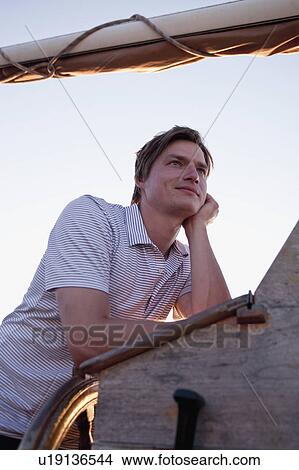 Picture - man standing at wooden steering wheel. Fotosearch