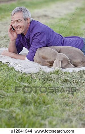 Picture - man with dog on the phone in the grass. Fotosearch