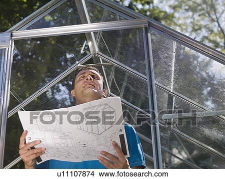 Picture - Man with greenhouse plans in garden. Fotosearch