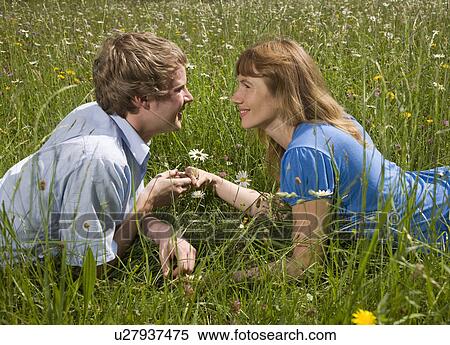 Stock Photography - man, woman lying in grass with flowers. Fotosearch