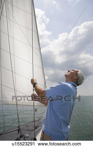 Stock Image - Mature man checking sails on yacht. Fotosearch